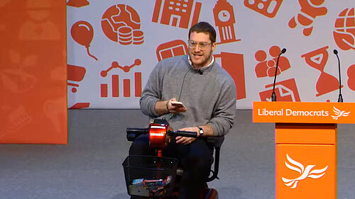 Jonah Weisz in wheelchair at Party Conference speaker podium